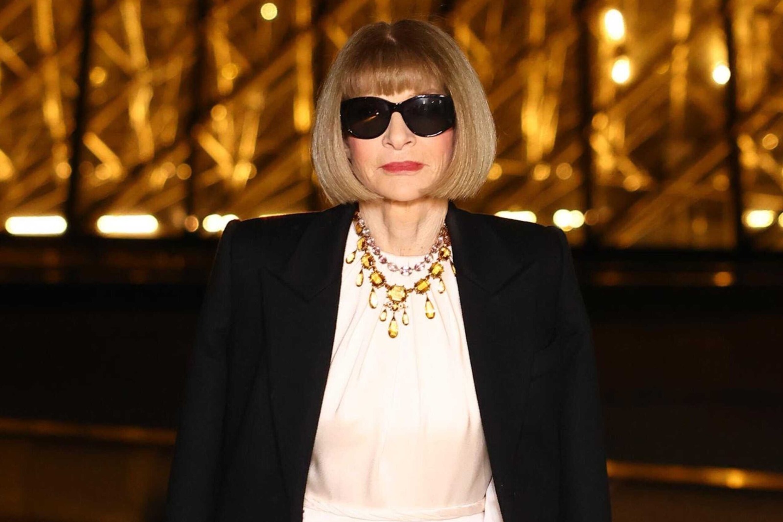 Anna Wintour con gafas oscuras y collar dorado, en un evento de moda internacional.