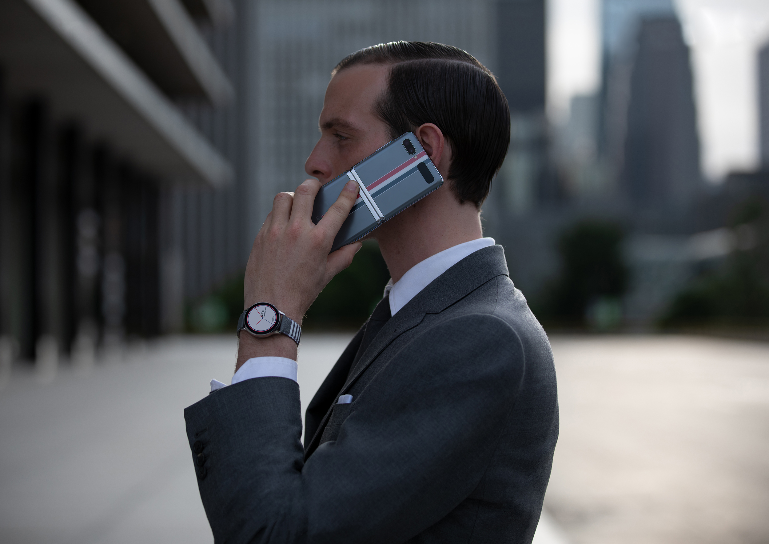 Hombre de negocios usando un smartphone Galaxy Z Flip edición especial Thom Browne en una llamada telefónica, en un entorno urbano moderno.