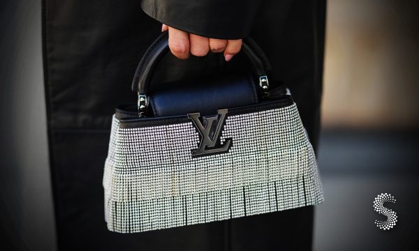 Bolso Louis Vuitton con incrustaciones de cristales plateados y asa corta, sostenido por una persona con abrigo negro