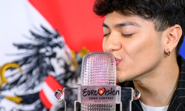 Ganador de Eurovisión 2025 besando el trofeo frente a la bandera de Austria