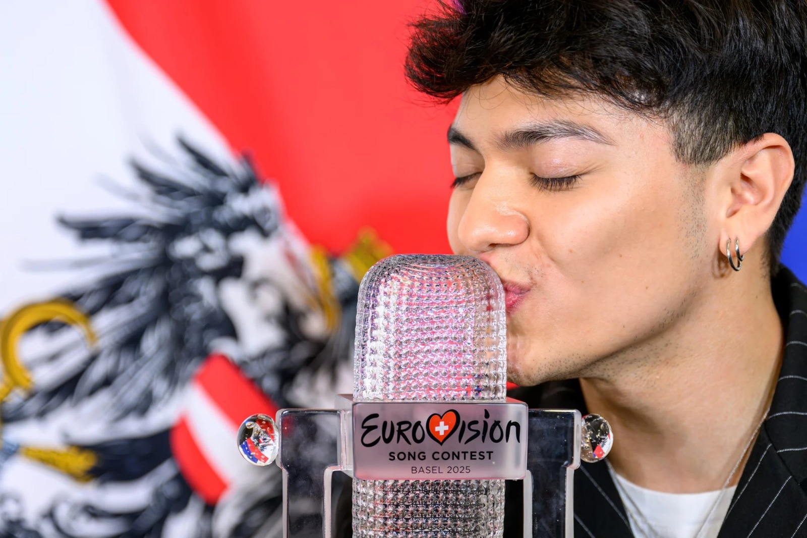 Ganador de Eurovisión 2025 besando el trofeo frente a la bandera de Austria