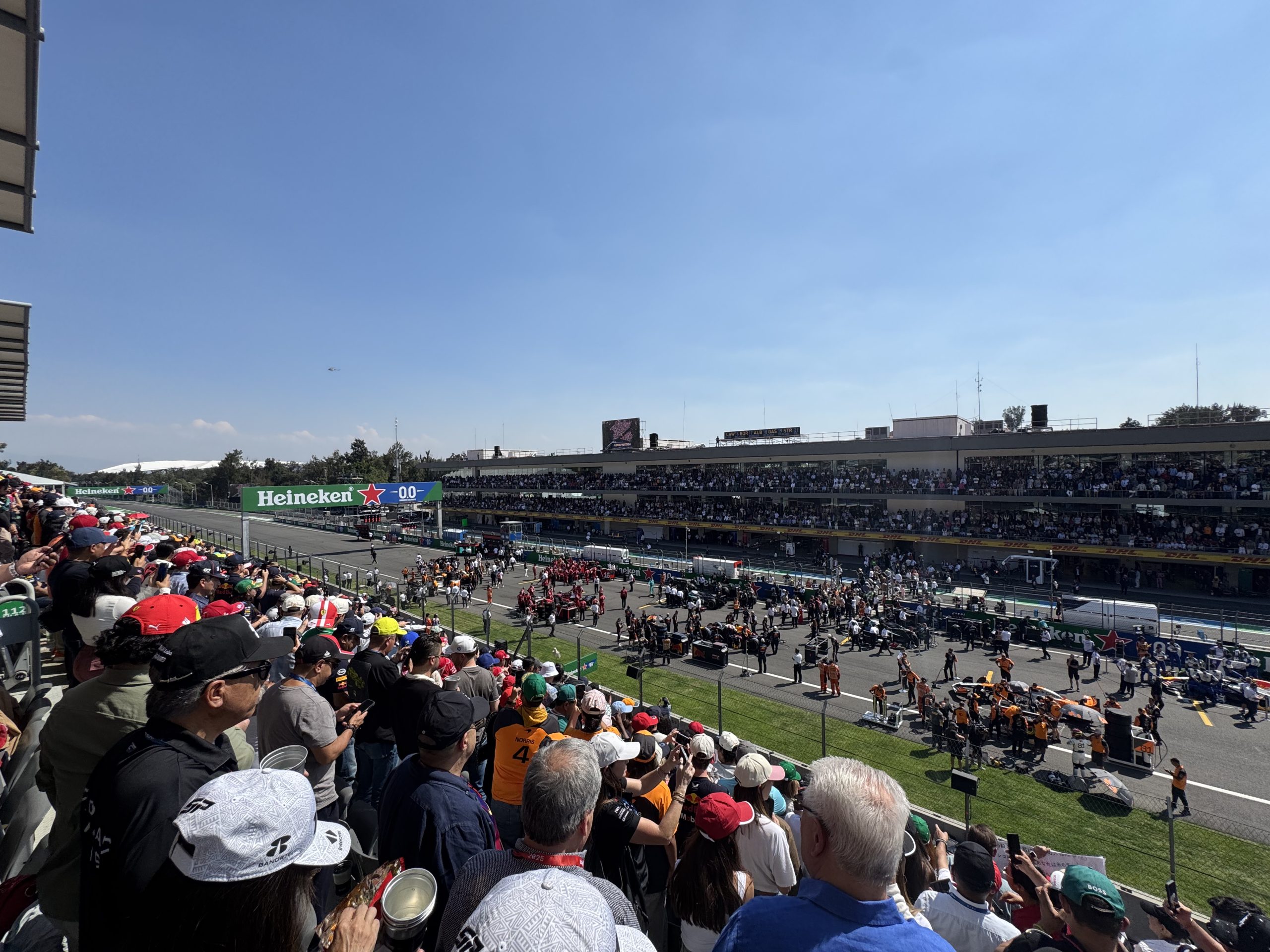 Vista panorámica del Autódromo Hermanos Rodríguez durante el Gran Premio de México de Fórmula 1, con gradas llenas y equipos preparando la salida en la pista.
